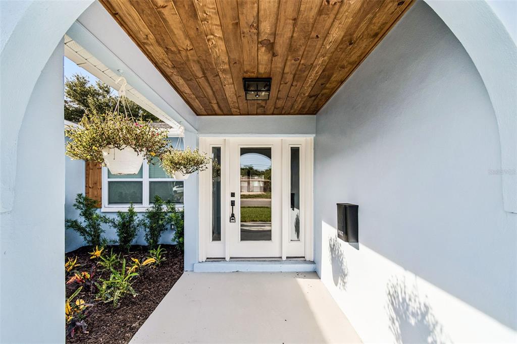 A covered entryway features a wood-paneled ceiling, a white front door, and hanging planters — 1101 54TH AVENUE S, ST PETERSBURG, FL