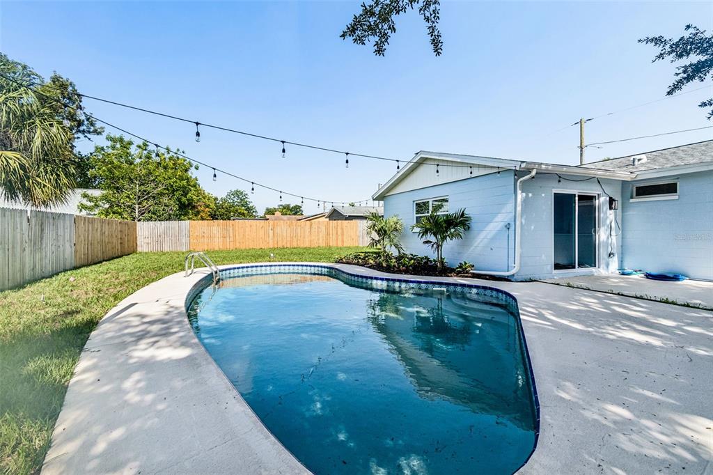 A backyard features a kidney-shaped swimming pool, a light blue house, and a wooden fence — 1101 54TH AVENUE S, ST PETERSBURG, FL