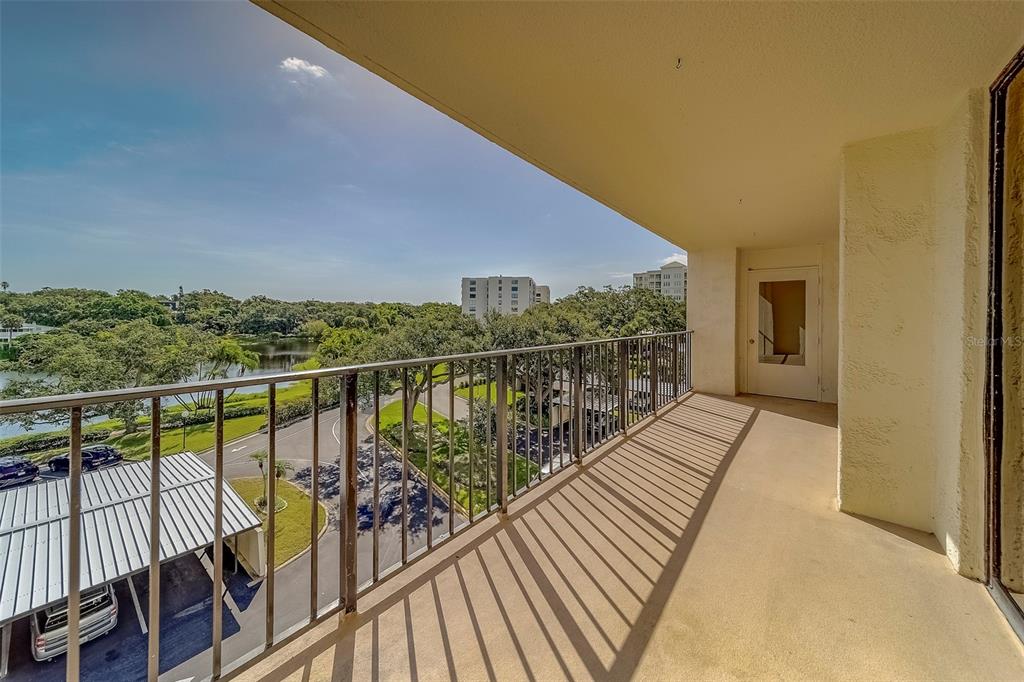 A covered balcony with a metal railing overlooks a parking area, trees, and a lake — 100 OAKMONT LANE UNIT 504, BELLEAIR, FL