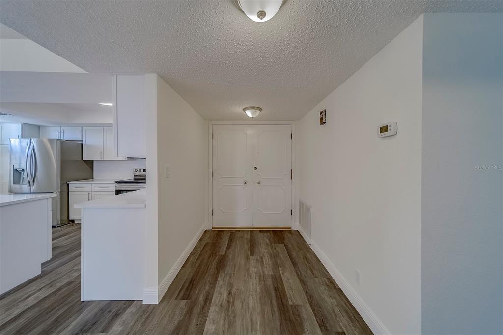 An entryway with wood-look flooring leads to double doors next to a white kitchen — 100 OAKMONT LANE UNIT 504, BELLEAIR, FL