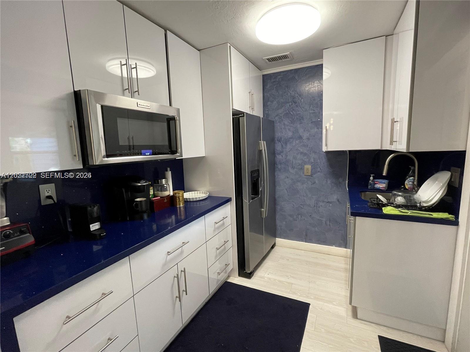 A kitchen features white cabinets, blue countertops, stainless steel appliances, and a textured blue wall — 1640 N 70th Way, Hollywood FL 33024, HOLLYWOOD, FL