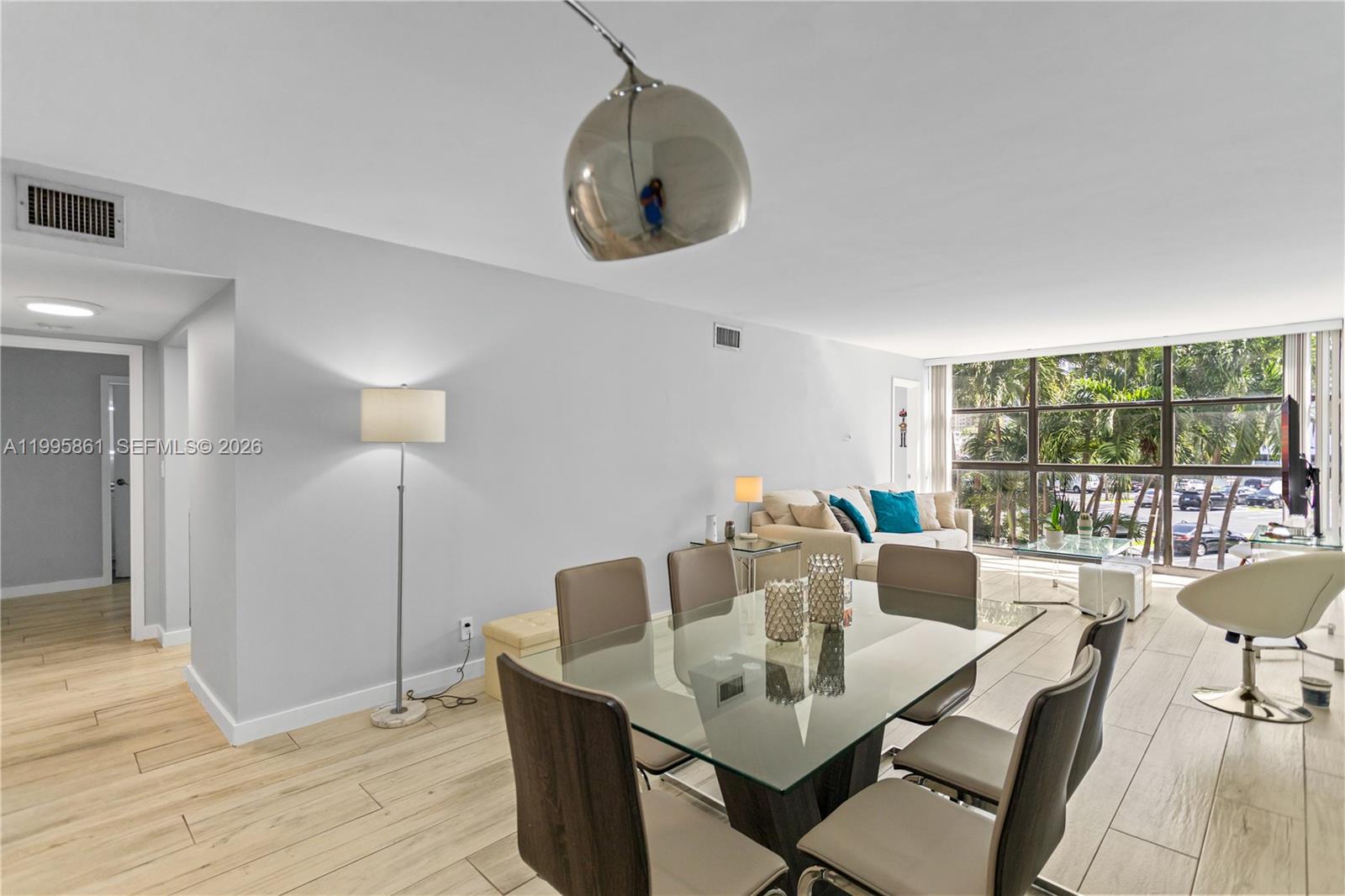 A dining area with a glass table and chairs sits in front of a living room — 600 Parkview Dr # 204, Hallandale Beach FL 33009, HALLANDALE BEACH, FL
