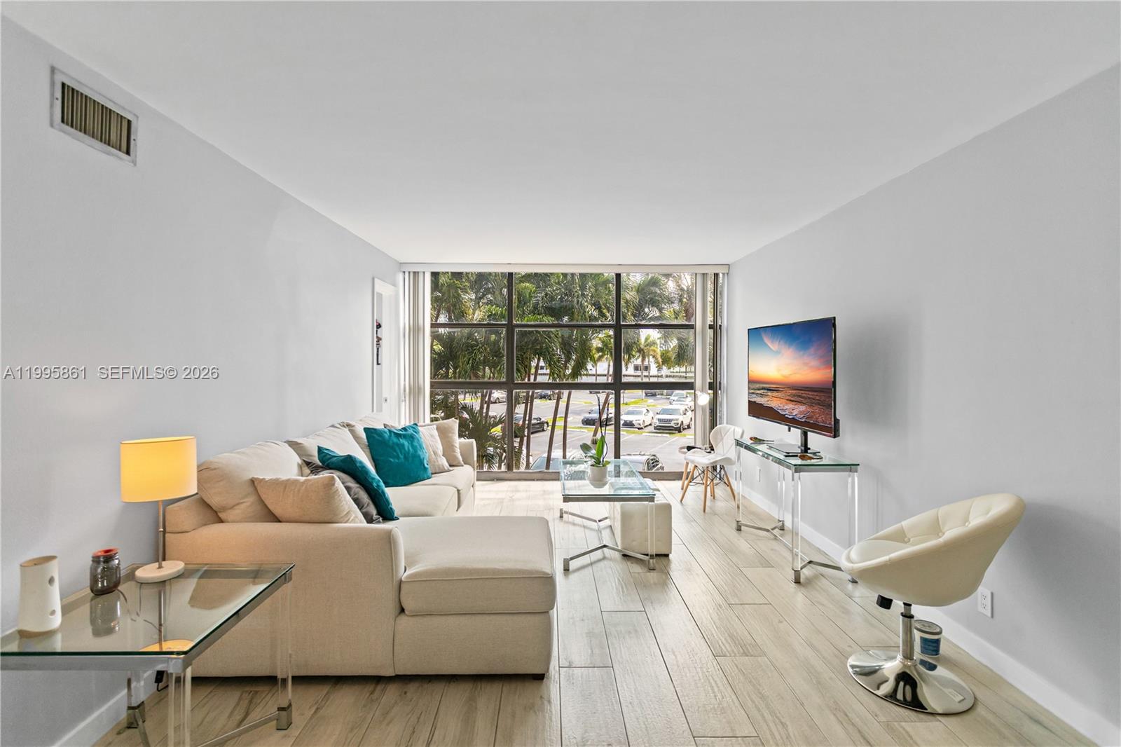 A living room features a beige sectional sofa, glass tables, and a wall-mounted television — 600 Parkview Dr # 204, Hallandale Beach FL 33009, HALLANDALE BEACH, FL