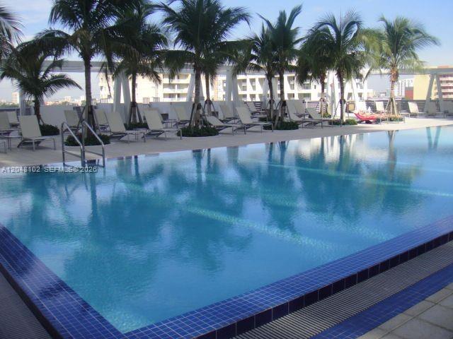 A swimming pool with blue tiles is surrounded by lounge chairs and palm trees — 1111 SW 1st Ave, Miami FL 33130, MIAMI, FL