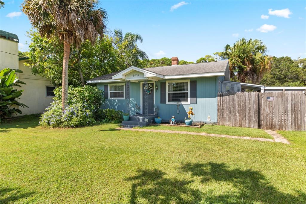 A single-story blue house with a front porch, lawn, and wooden fence under a blue sky — 6030 62ND STREET N, ST PETERSBURG, FL