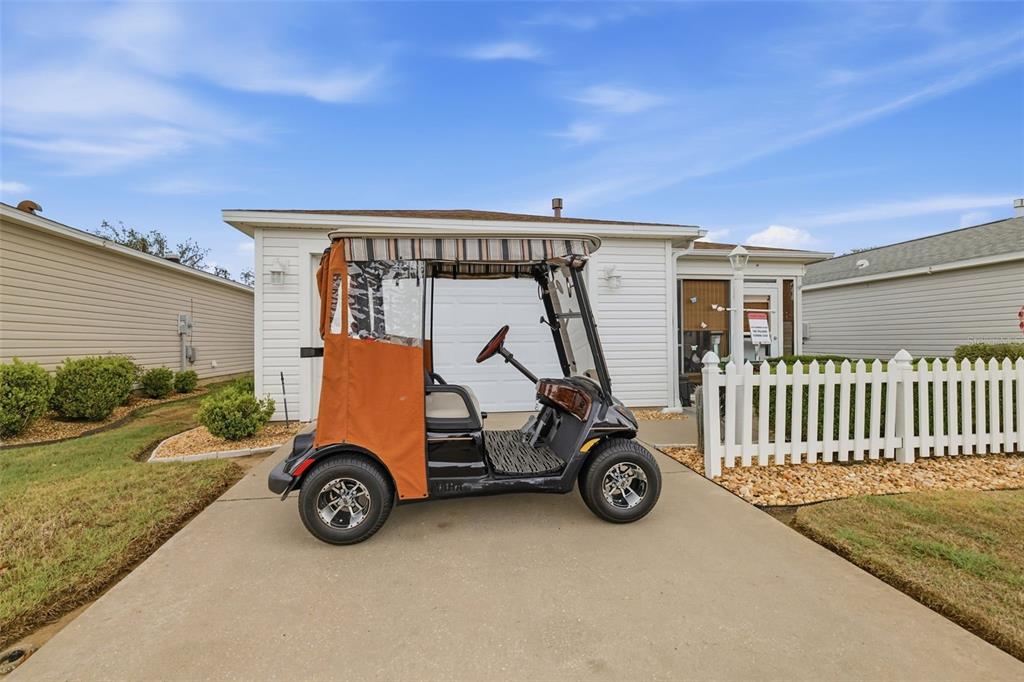 A golf cart is parked on the concrete driveway in front of a white house — 1639 S ALLENDALE PLACE, THE VILLAGES, FL