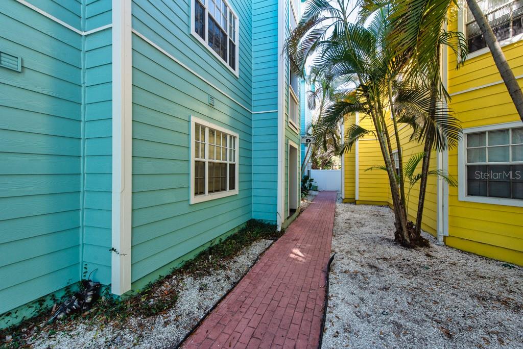 A brick walkway leads between a teal building and a yellow building with palm trees — 3002 W CLEVELAND STREET UNIT D11, TAMPA, FL