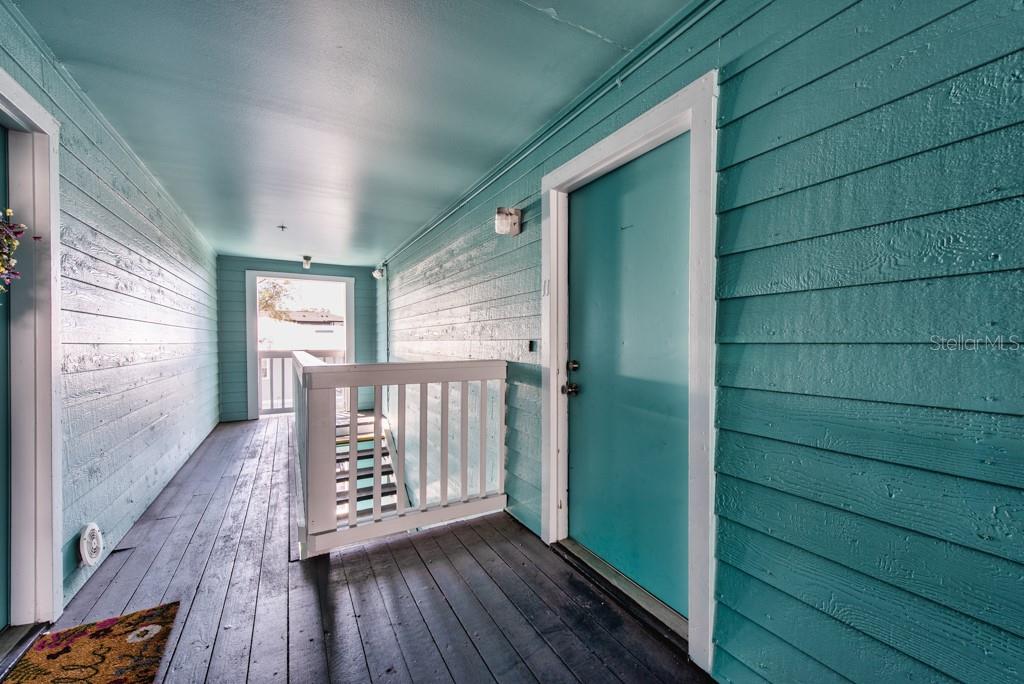 An outdoor covered walkway features teal wood siding, a dark deck, and a white railing — 3002 W CLEVELAND STREET UNIT D11, TAMPA, FL