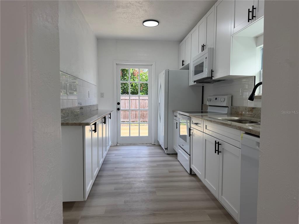 A galley kitchen features white cabinets, granite countertops, stainless steel appliances, and a glass-paned door — 1102 E 108TH AVENUE, TAMPA, FL