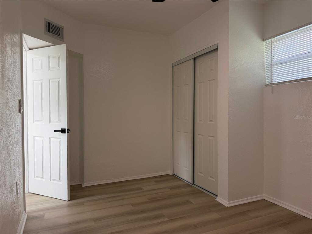 An empty bedroom features white walls, light wood-look flooring, a closet, and an open door — 1102 E 108TH AVENUE, TAMPA, FL
