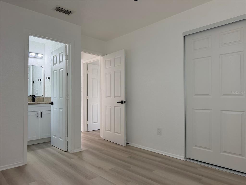 A bedroom features light wood-look flooring, white walls, a sliding closet, and two open doors — 1102 E 108TH AVENUE, TAMPA, FL
