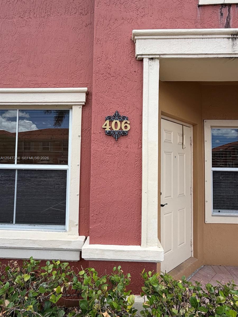 The exterior of a building features a red stucco wall with a house number 406 plaque — 6016 NW 116th Pl # 406, Doral FL 33178, DORAL, FL