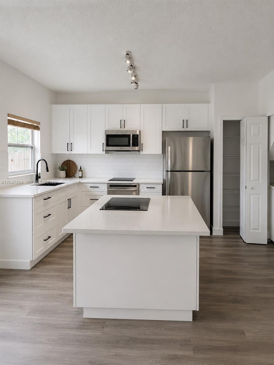 A modern kitchen features white cabinets, stainless steel appliances, a center island, and wood flooring — 6016 NW 116th Pl # 406, Doral FL 33178, DORAL, FL