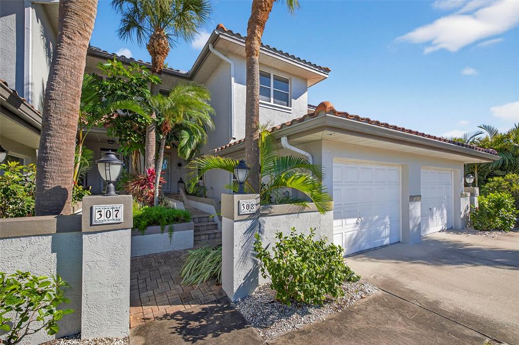 The exterior of a two-story residential building features a paved walkway, palm trees, and garages — 903 PINELLAS BAYWAY S UNIT 308, TIERRA VERDE, FL
