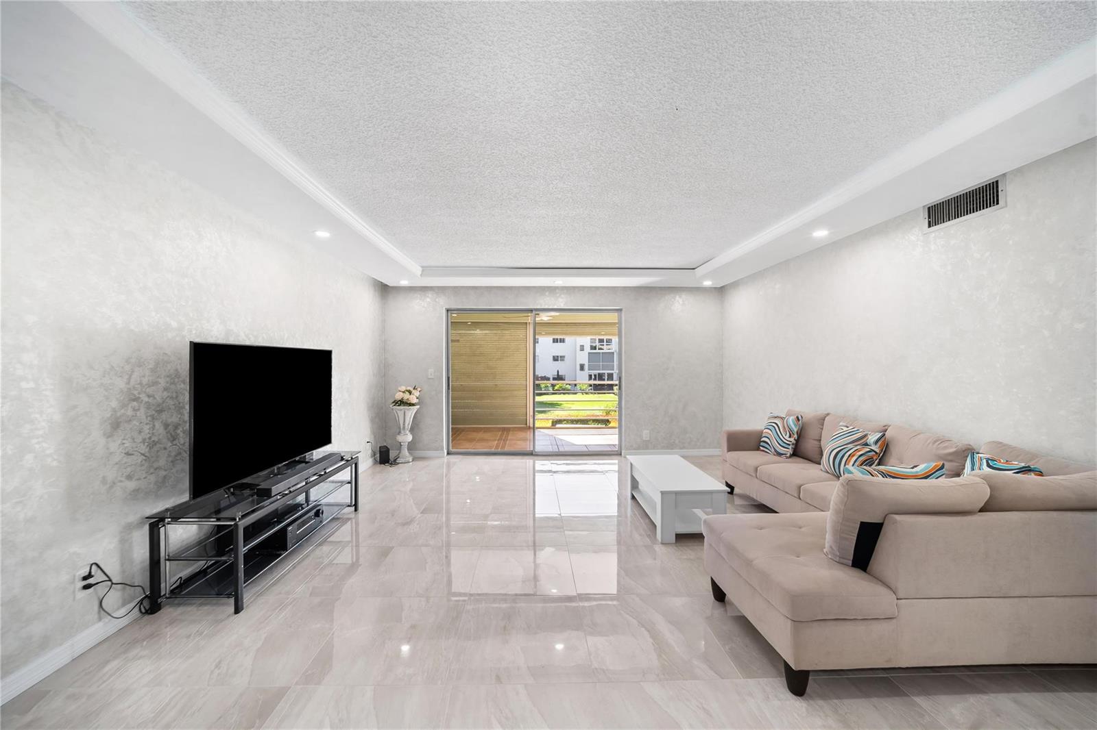 A living room features light-colored tile floors, textured walls, a sectional sofa, and sliding doors — 2615 NE 3rd Court # 220, Boynton Beach FL 33435, BOYNTON BEACH, FL