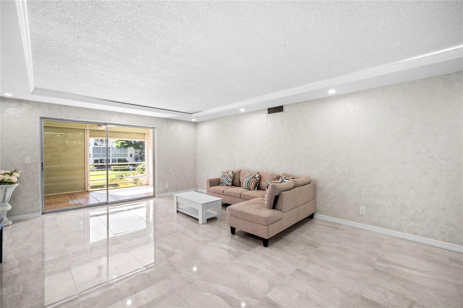 A living room features light-colored tile flooring, a beige sectional sofa, and a sliding glass door — 2615 NE 3rd Court # 220, Boynton Beach FL 33435, BOYNTON BEACH, FL