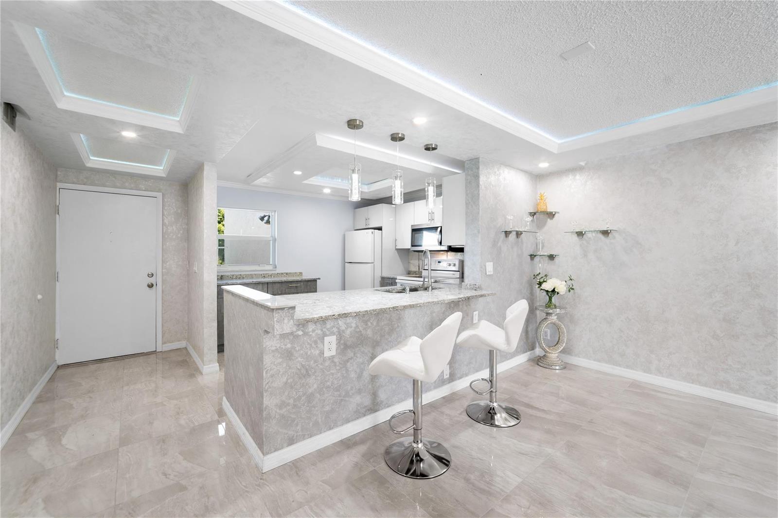 A modern kitchen features a granite breakfast bar, white bar stools, and grey textured walls — 2615 NE 3rd Court # 220, Boynton Beach FL 33435, BOYNTON BEACH, FL