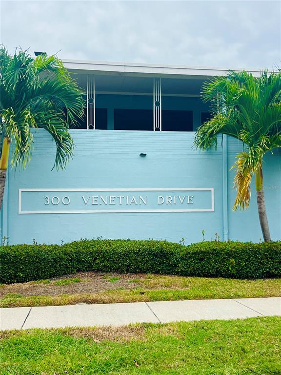 A light blue building exterior features a sign with the address and two palm trees — 300 VENETIAN DRIVE UNIT 2, CLEARWATER, FL