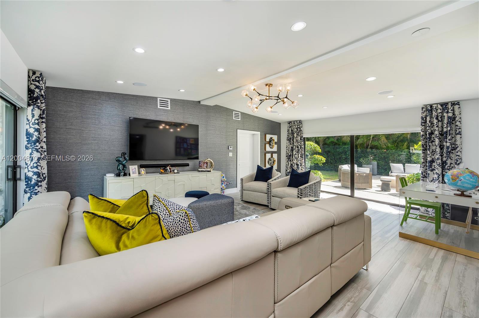 A modern living room features a large sectional sofa, gray textured wallpaper, and sliding glass doors — 831 Cortez St, Coral Gables FL 33134, CORAL GABLES, FL