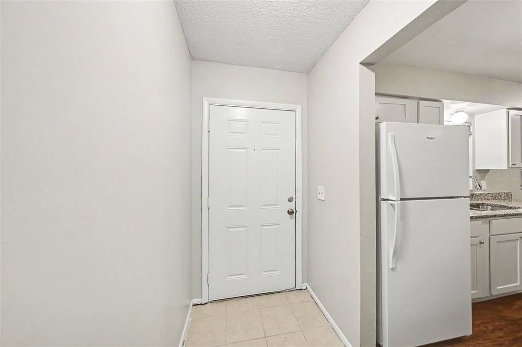 A white front door opens into a small entryway with tile flooring next to a kitchen — 702 GREGORY COURT, ALTAMONTE SPRINGS, FL