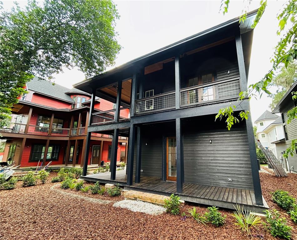 A two-story dark-painted house with a covered porch and balcony stands next to a red house — 296 NW 12TH AVENUE, GAINESVILLE, FL