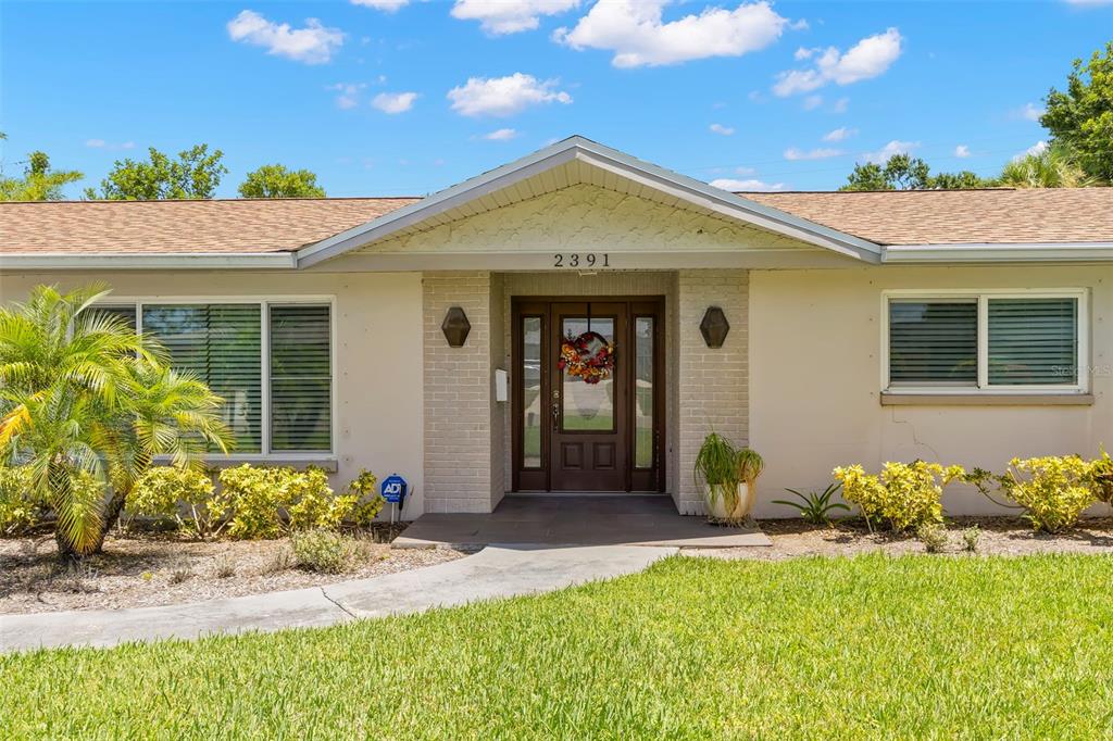A single-story house exterior features a brick entryway, a front door with a wreath, and landscaping — 2391 66TH TERRACE S, ST PETERSBURG, FL