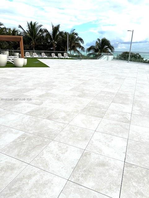 A large, light-colored stone patio overlooks a swimming pool area with palm trees and ocean views — 7135 Collins Ave # 722, Miami Beach FL 33141, MIAMI BEACH, FL