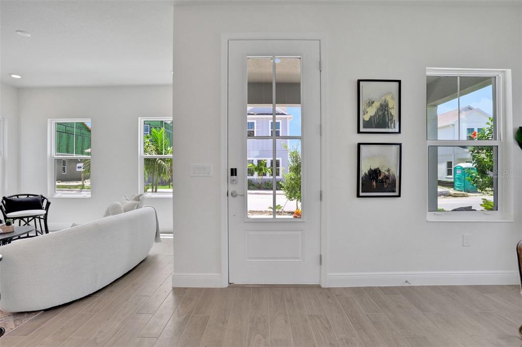 A bright living room features light wood flooring, a glass-paneled front door, and white walls — 9124 WALCOTT LANE, LAKEWOOD RANCH, FL