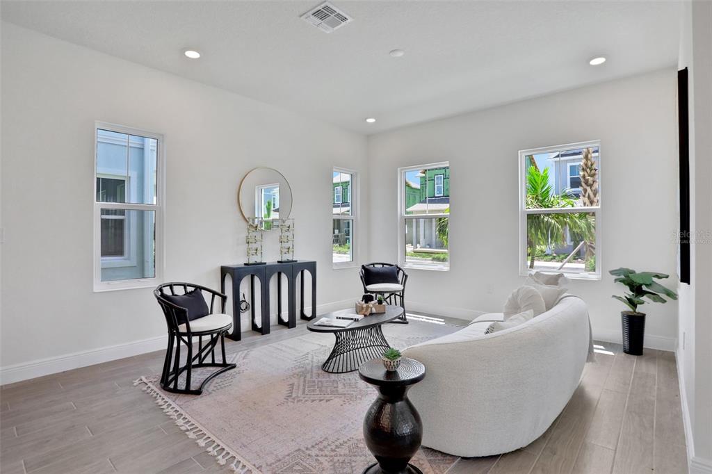 A bright living room features white walls, tile flooring, a curved sofa, and black furniture — 9124 WALCOTT LANE, LAKEWOOD RANCH, FL
