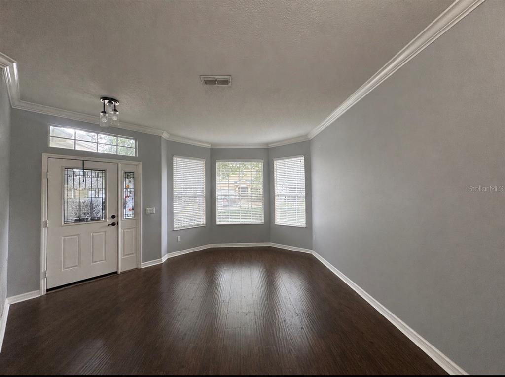 An empty room features gray walls, dark wood flooring, a bay window, and a front door — 15245 STONEBRIAR WAY, ORLANDO, FL