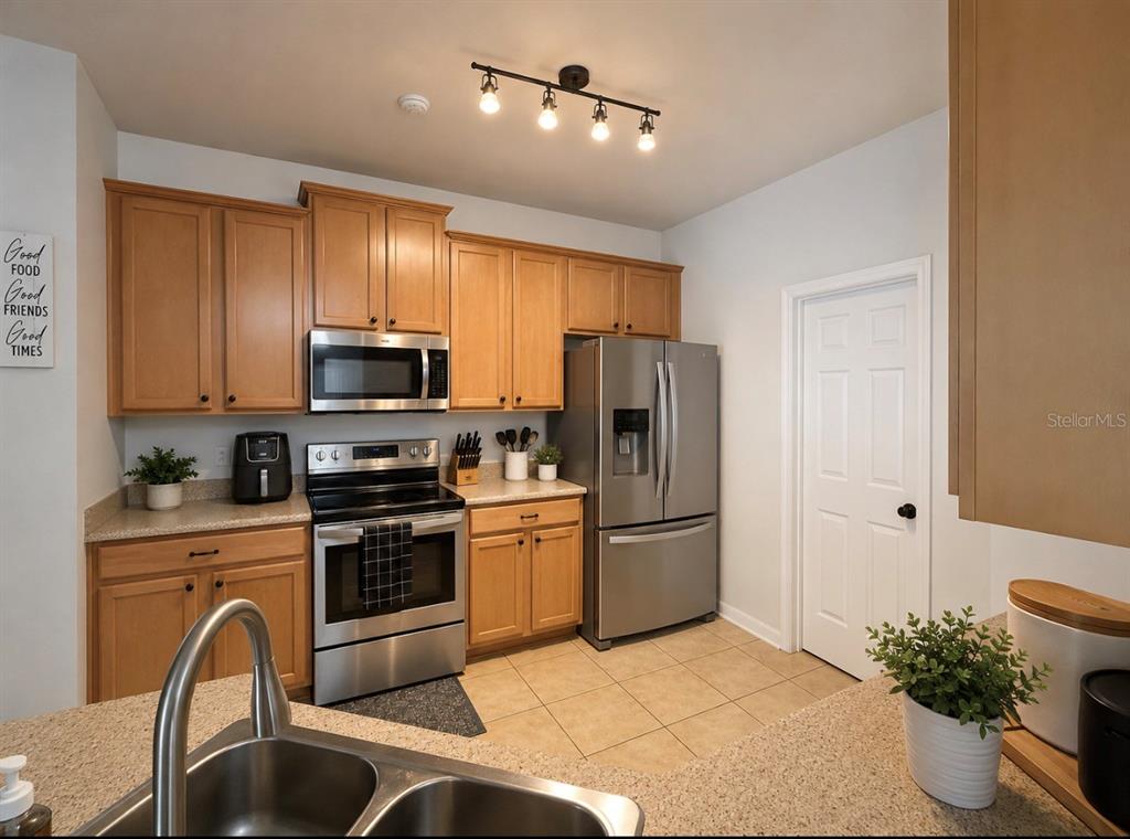 A kitchen features light wood cabinets, stainless steel appliances, and a tiled floor — 15245 STONEBRIAR WAY, ORLANDO, FL