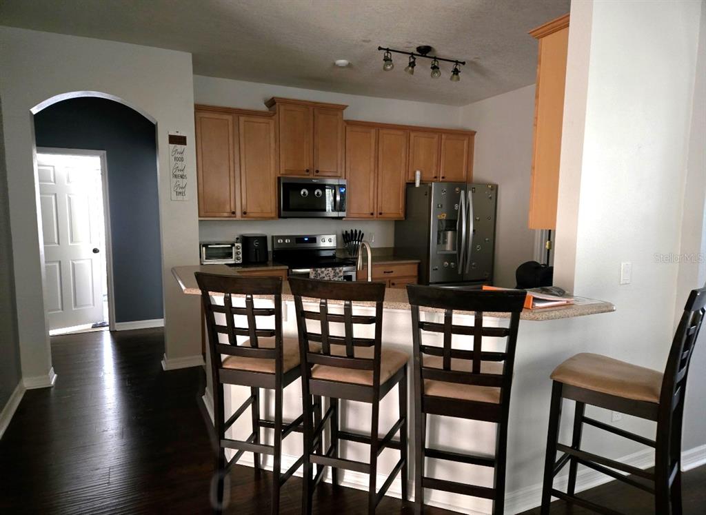 A kitchen features light wood cabinets, stainless steel appliances, and a breakfast bar with stools — 15245 STONEBRIAR WAY, ORLANDO, FL