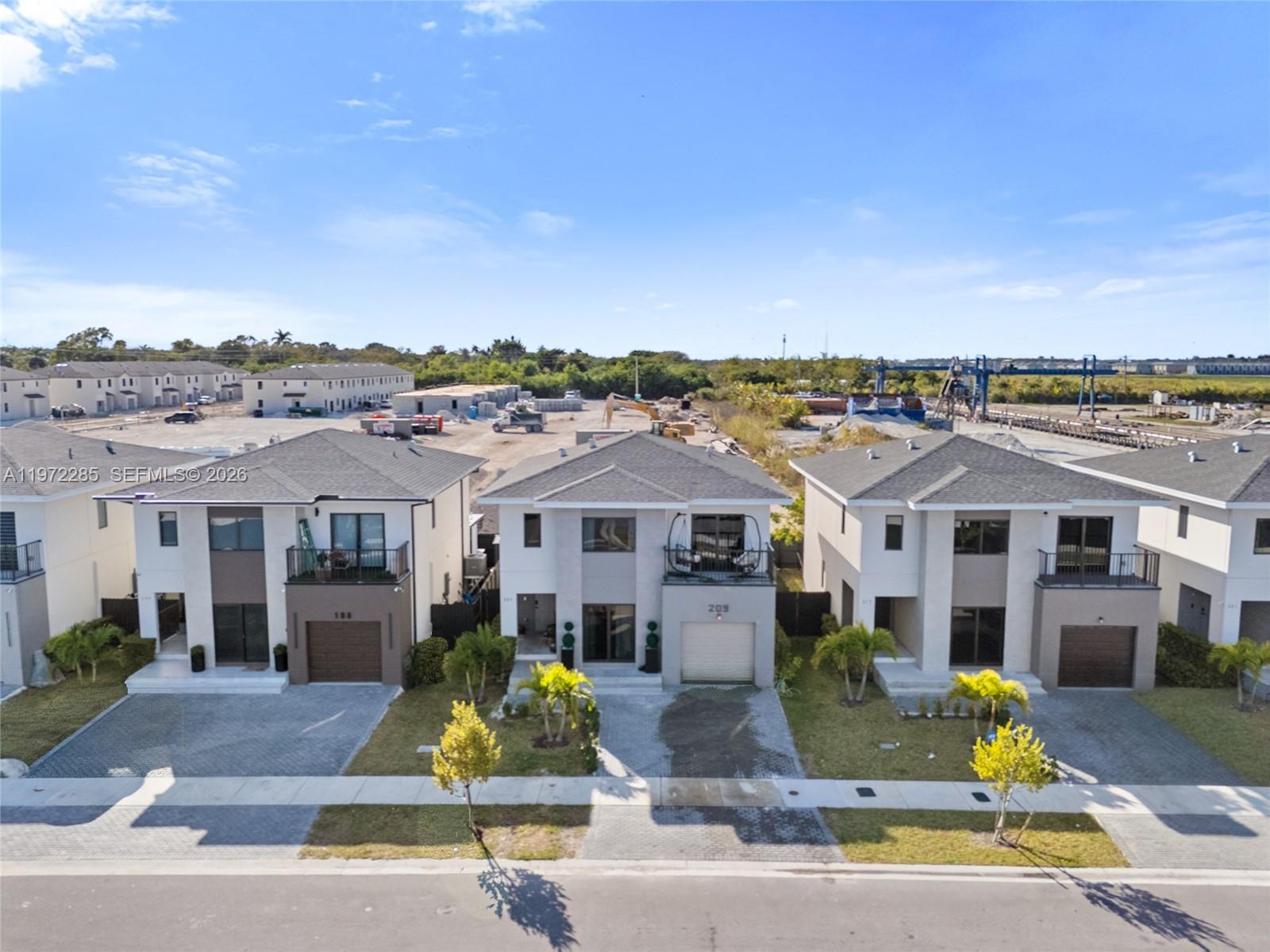Three modern two-story houses with attached garages stand along a paved street — 209 NW 13th Pl, Florida City FL 33034, FLORIDA CITY, FL