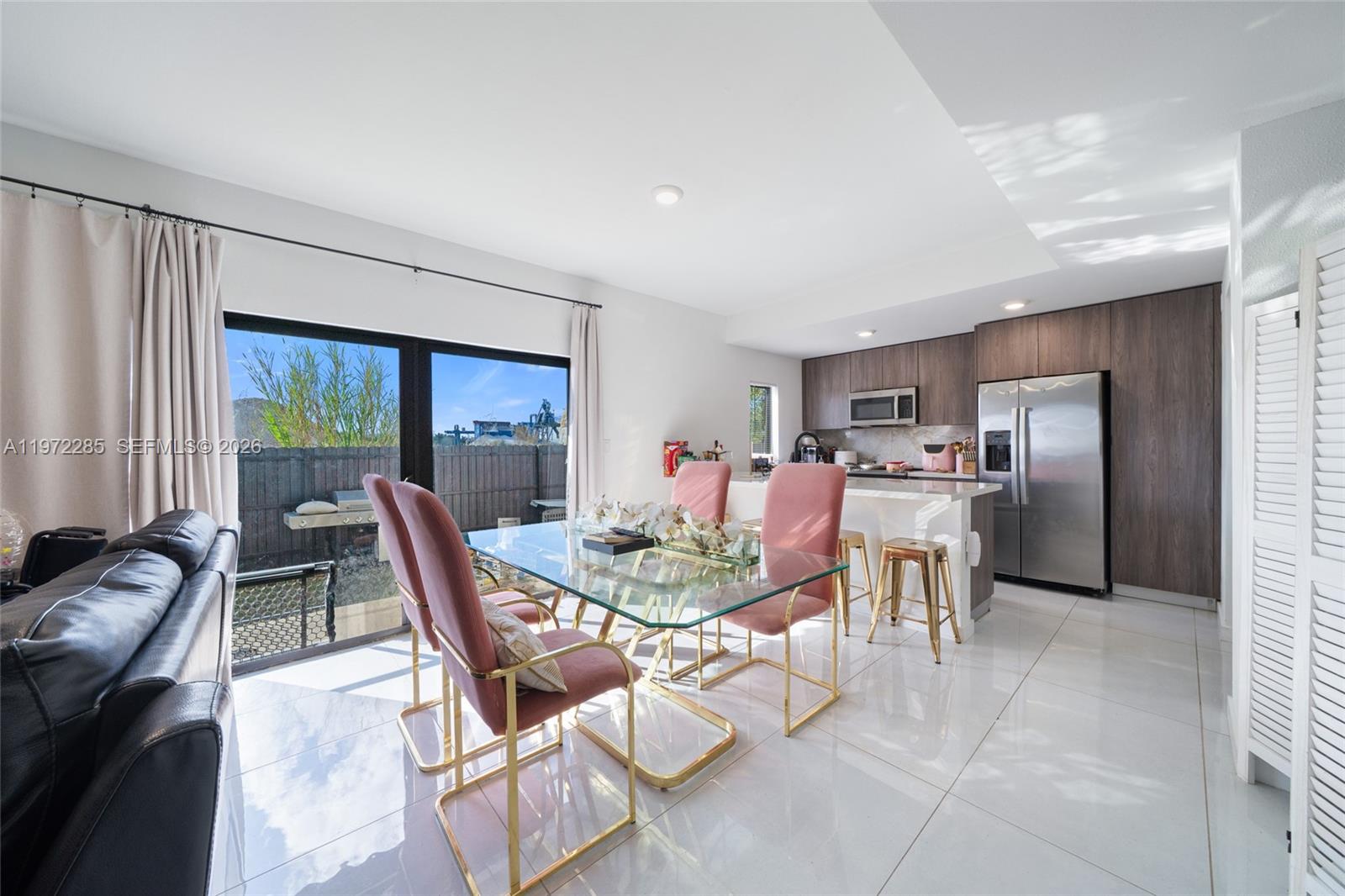 A dining area with a glass table and pink chairs sits adjacent to a modern kitchen — 209 NW 13th Pl, Florida City FL 33034, FLORIDA CITY, FL