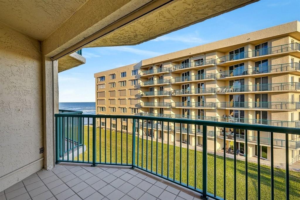 A tiled balcony with a green railing overlooks a grassy lawn and a beachside apartment building — 4555 S ATLANTIC AVENUE UNIT 4411, PORT ORANGE, FL