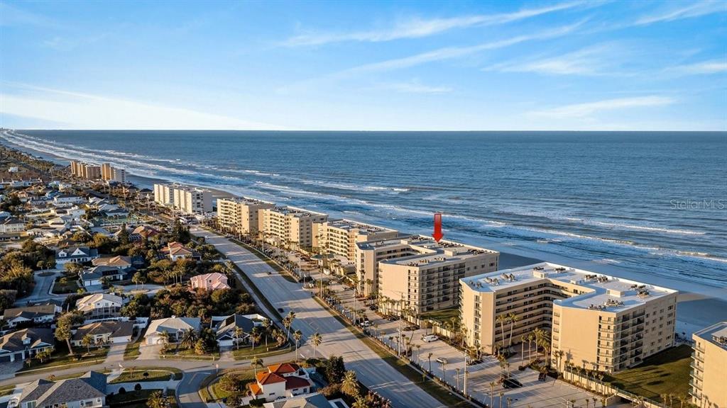 An aerial view shows beachfront condominium buildings along a coastline with a red arrow pointing down — 4555 S ATLANTIC AVENUE UNIT 4411, PORT ORANGE, FL