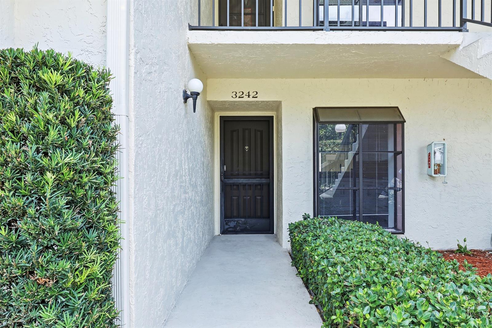 The exterior view shows a ground-level apartment entrance with a dark door and landscaping — 3242 Perimeter Drive, FL 33467, FL
