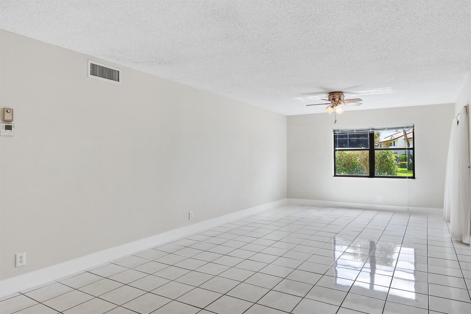 An empty room features white tiled floors, light-colored walls, a ceiling fan, and a window — 3242 Perimeter Drive, FL 33467, FL