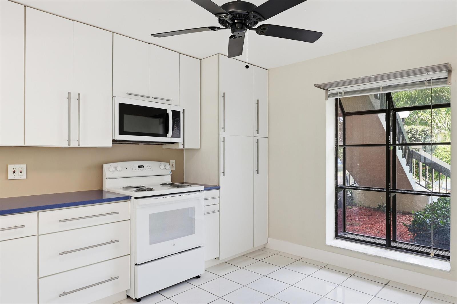 A kitchen with white cabinets, a white stove, blue countertops, and a large window — 3242 Perimeter Drive, FL 33467, FL