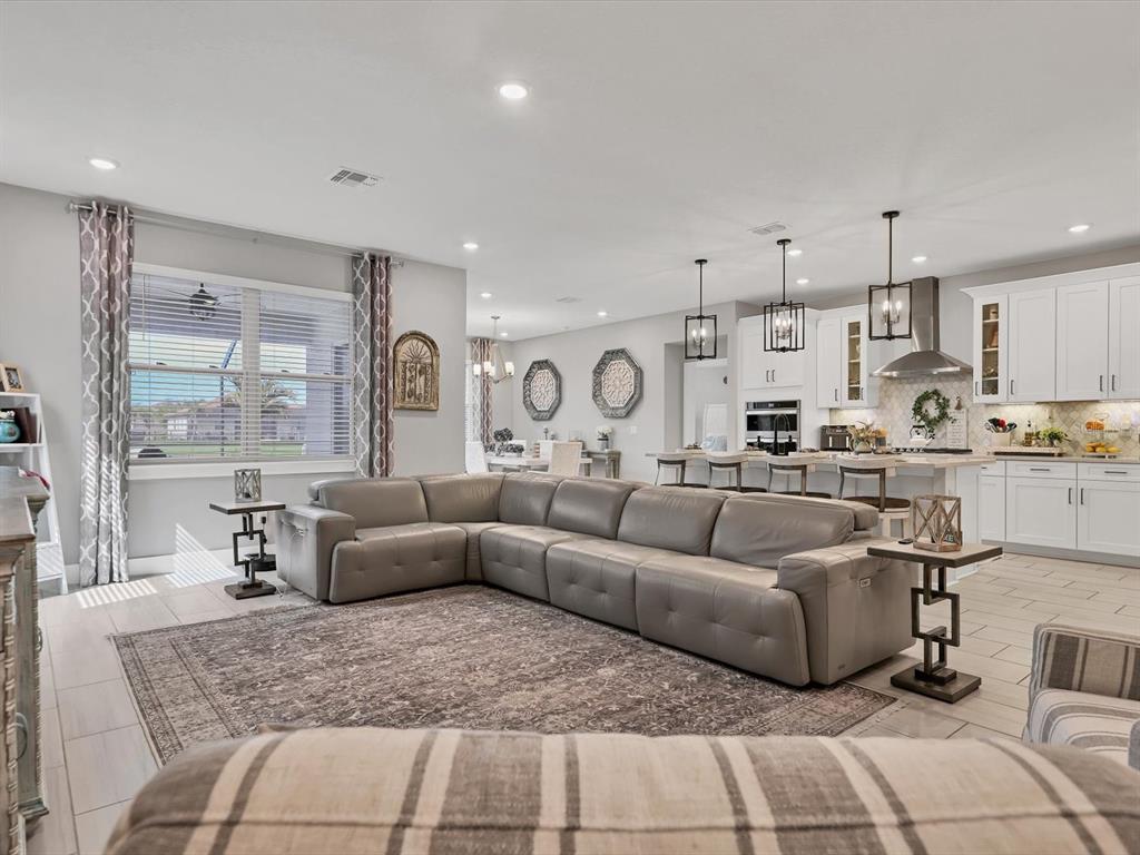An open-concept living room features a large gray sectional sofa, tile flooring, and a kitchen — 13925 GREEN HAMMOCK PLACE, BRADENTON, FL