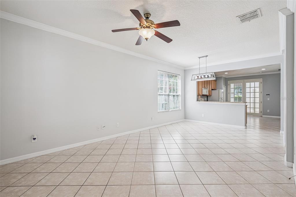 A spacious room with light tile flooring, a ceiling fan, and an open kitchen view — 5451 KUMQUAT LOOP, WINDERMERE, FL
