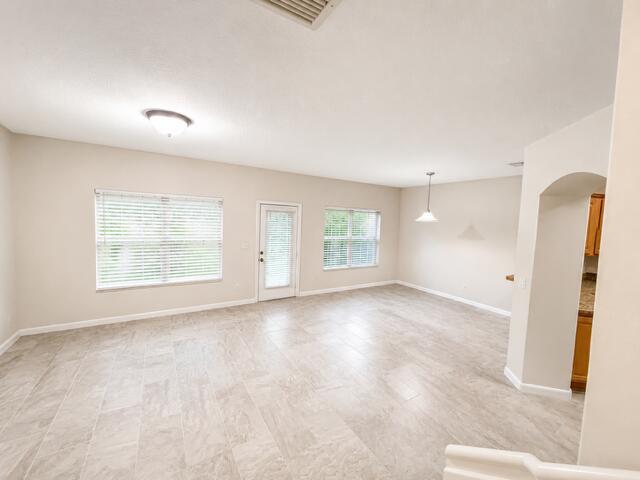 A bright, empty living room features light-colored tile flooring, beige walls, and two windows — 4406 NE Windmill Palm Way, FL 33463, FL