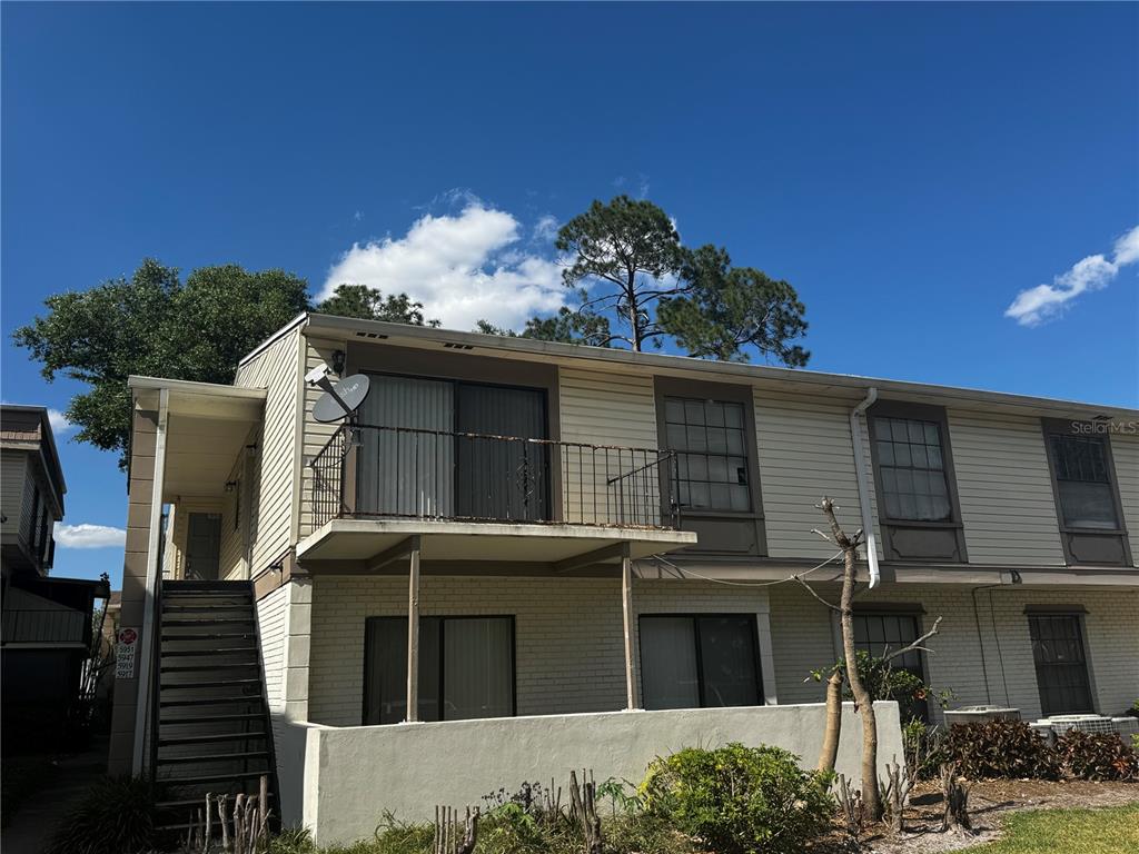 A two-story apartment building features a second-floor balcony, exterior stairs, and light-colored siding — 5917 VILLAGE CIRCLE UNIT 5917, ORLANDO, FL