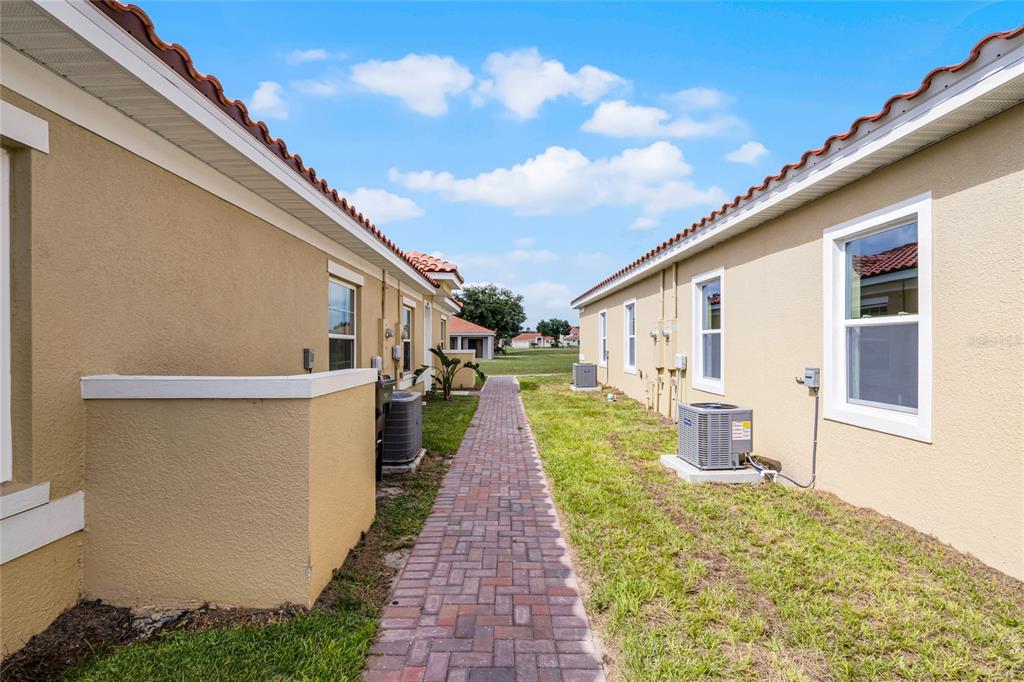 A brick walkway leads between two tan stucco buildings with air conditioning units and windows — 1822 CORIANDER DRIVE, KISSIMMEE, FL