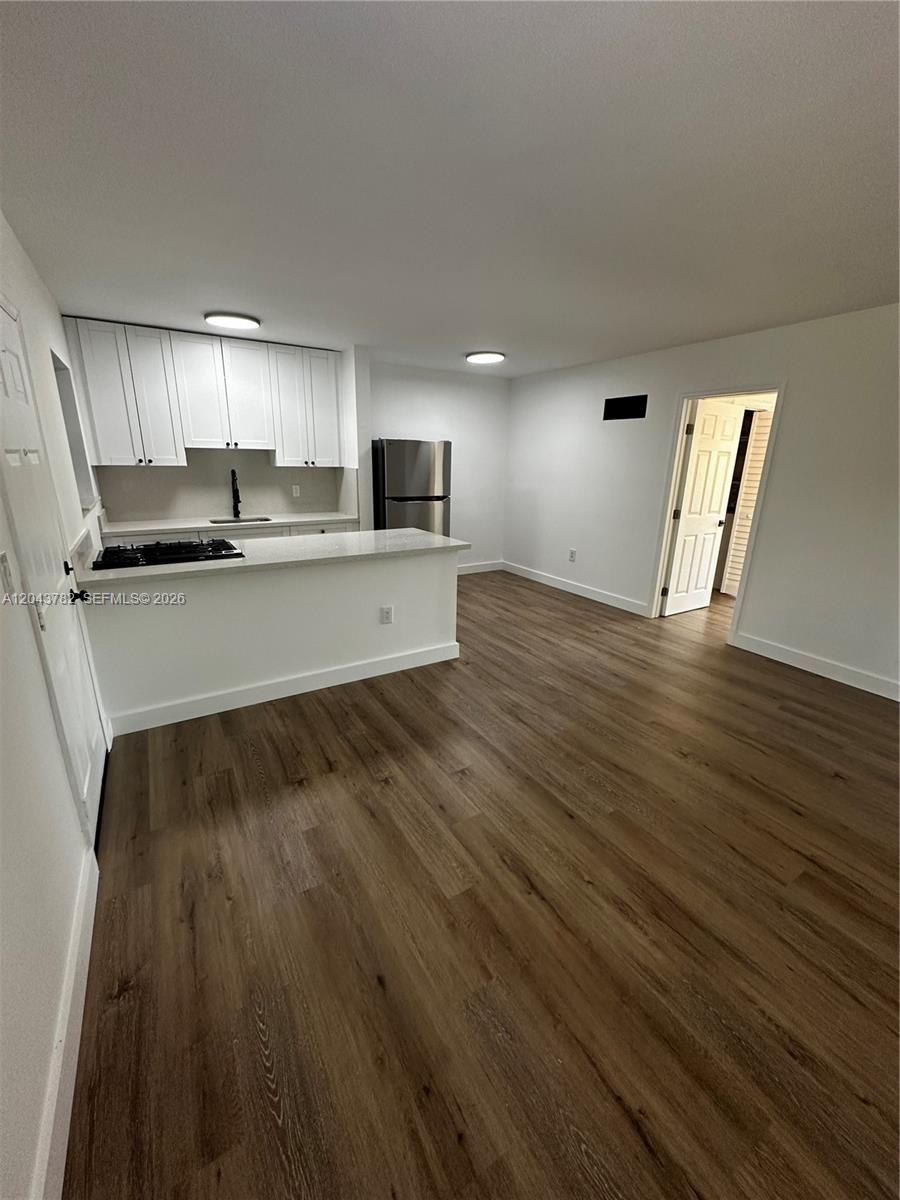A kitchen with white cabinets and a breakfast bar opens into a living area — 1255 W 49th Pl # E205, Hialeah FL 33012, HIALEAH, FL