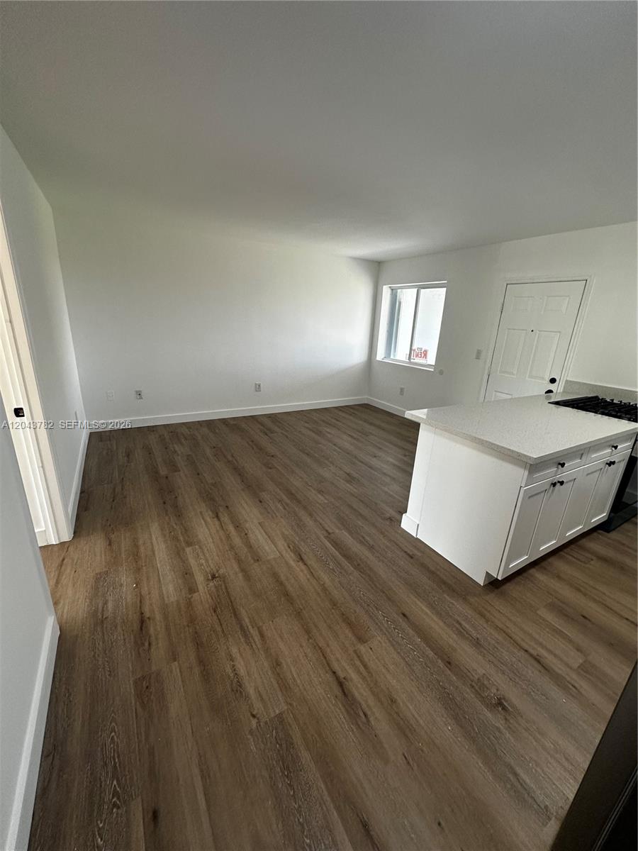An open-concept living area features wood-look flooring, white walls, and a kitchen island — 1255 W 49th Pl # E205, Hialeah FL 33012, HIALEAH, FL