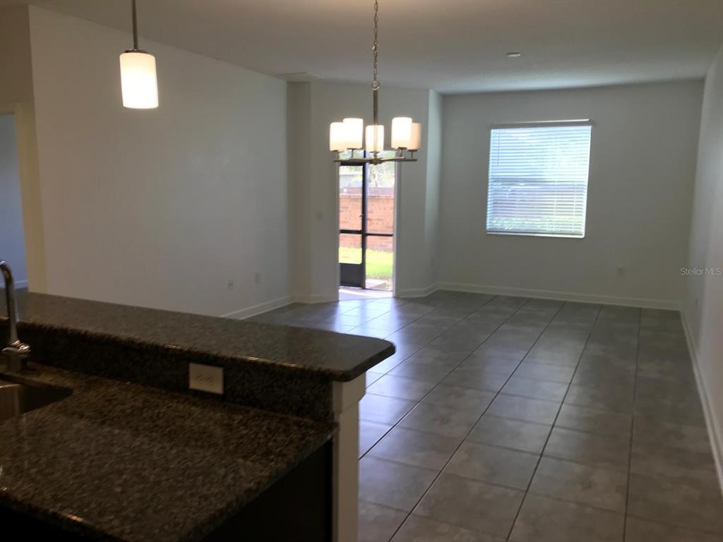 A kitchen counter with granite countertops overlooks a dining area with tile floors and lighting — 3348 RODRICK CIRCLE, ORLANDO, FL