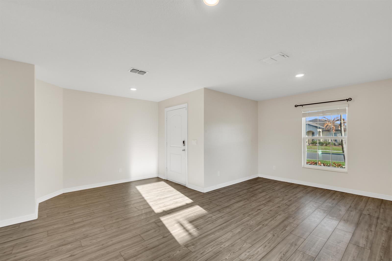 An empty room features light-colored walls, wood-look flooring, a white door, and a single window — 5532 Imagination Drive, Fort Pierce FL 34947, FORT PIERCE, FL