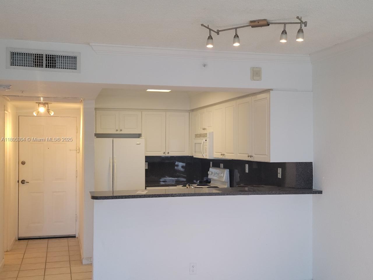 A kitchen with white cabinets, dark countertops, and a breakfast bar overlooks a tiled entryway — 2501 S Ocean Dr # 1634, Hollywood FL 33019, HOLLYWOOD, FL