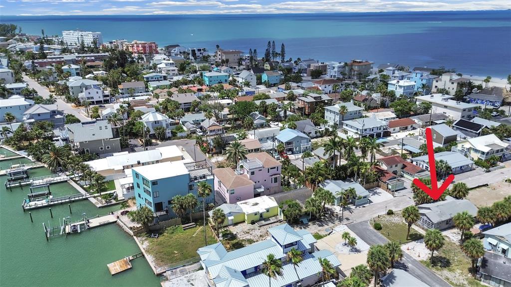 An aerial view shows a coastal neighborhood with a red arrow pointing to a house — 130 90TH AVENUE, TREASURE ISLAND, FL